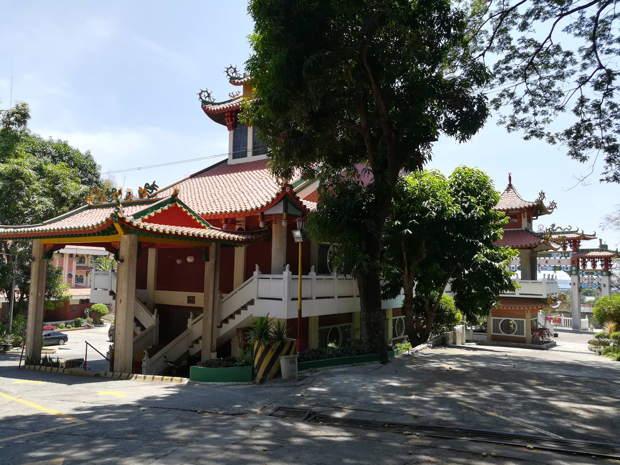 Side view of Ma-Cho Temple in San Fernando, La Union, featuring traditional Chinese architecture with red-tiled roofs and white staircases amidst lush greenery.