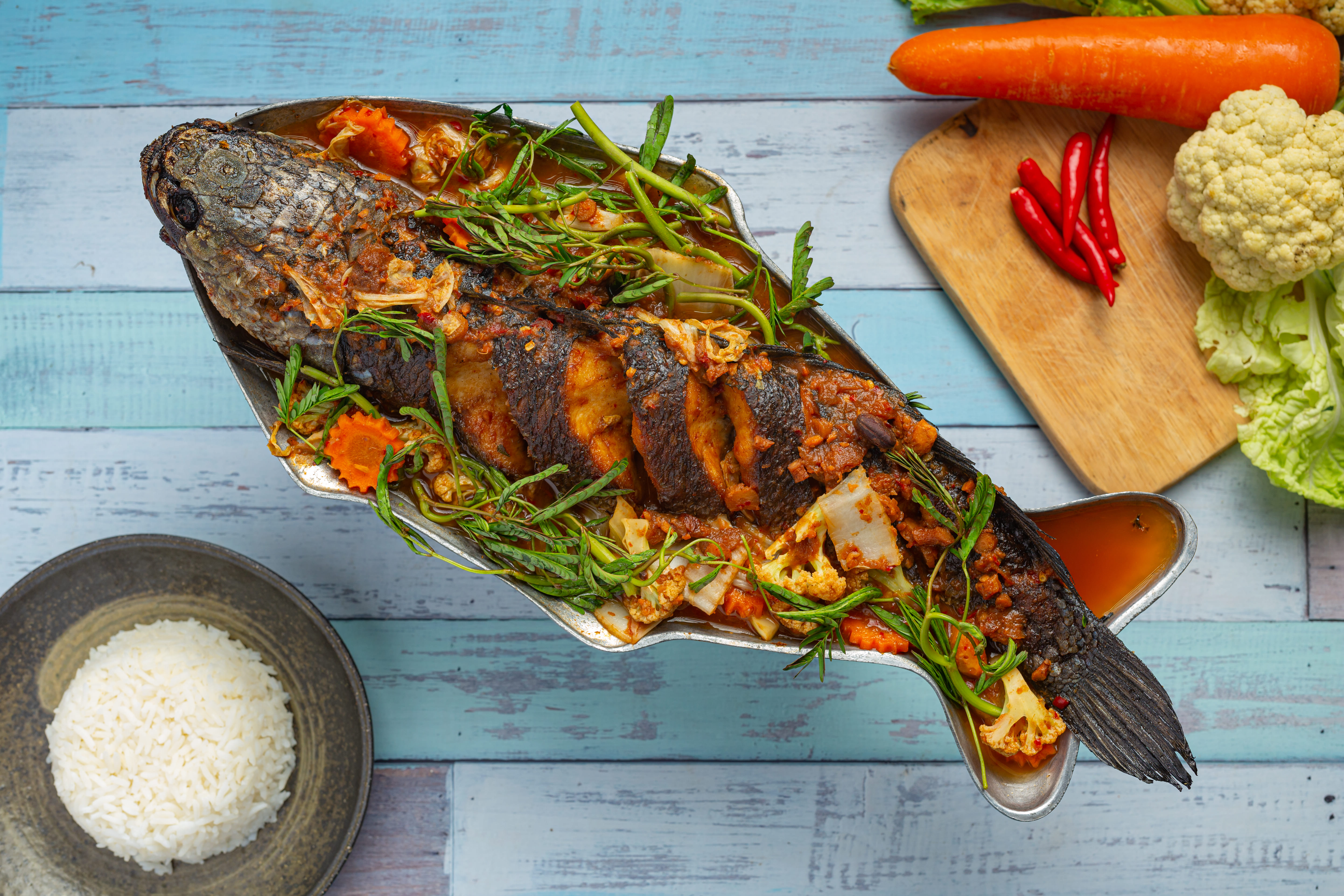 Ikan Bakar, a grilled fish dish, served with herbs, vegetables, and rice on a metal tray, prepared at a warung near Mawun Beach in Lombok, Indonesia.