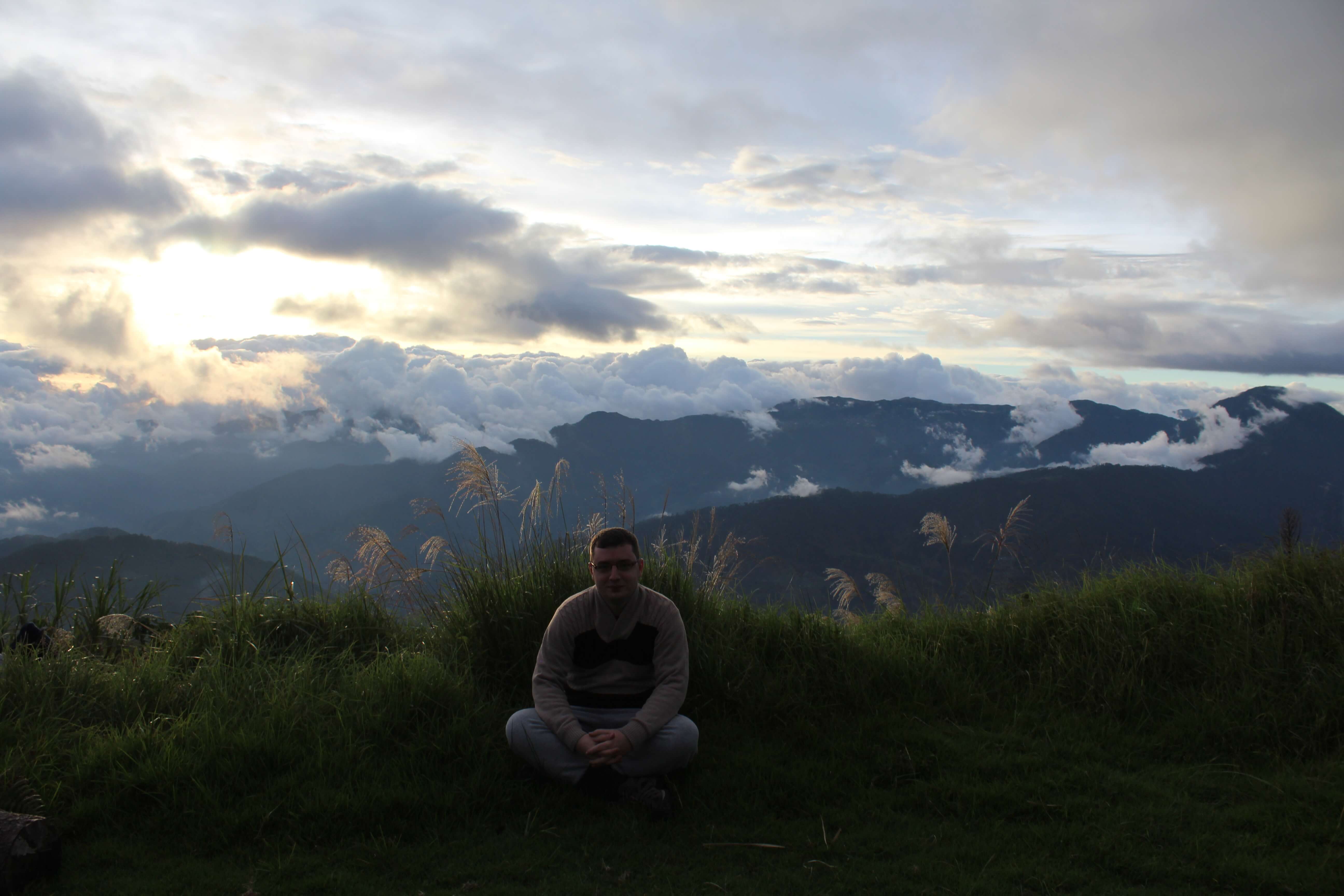 Hiker sitting on Mount Pulag with sea of clouds and sunrise over rolling hills, 2025