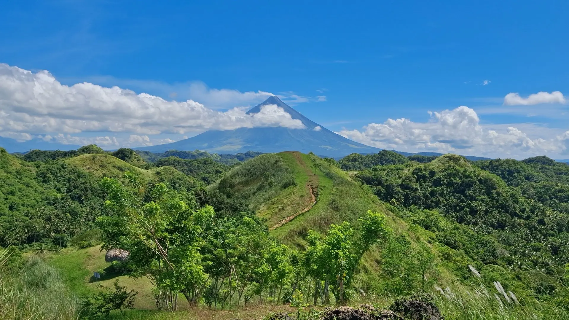 The iconic Mount Mayon looming majestically behind the rolling emerald peaks of Quitinday Hills